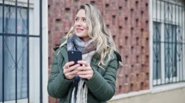 Sokakta akıllı telefon kullanan, kendine güvenen genç sarışın kadın.