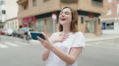 Sokakta akıllı telefondan video seyreden kendine güvenen genç bir kadın.