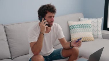 Genç İspanyol adam elinde kredi kartıyla akıllı telefondan konuşuyor.