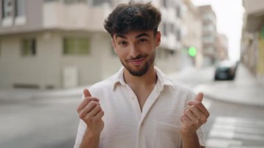 Young arab man smiling confident doing spend money gesture at street