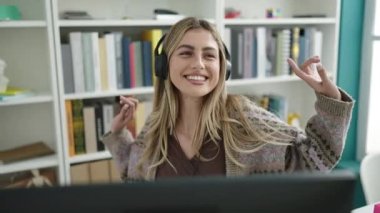 Genç sarışın kız öğrenci kendinden emin bir şekilde gülümsüyor kütüphanede müzik dinliyor ve dans ediyor.