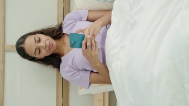 Young african american woman using smartphone sitting on bed at bedroom