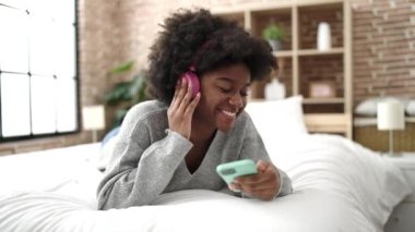 Afrika kökenli Amerikalı kadın dans ediyor ve yatakta müzik dinliyor.