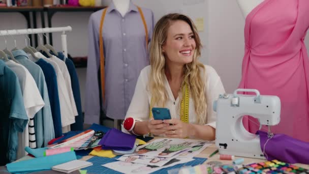 在裁缝店用智能手机自信地微笑着的金发女裁缝 — 图库视频影像