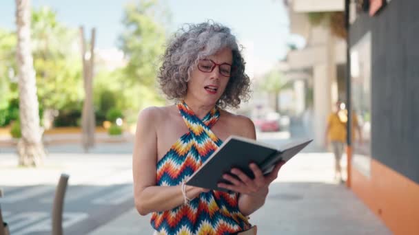 Mujer Pelo Gris Mediana Edad Sonriendo Libro Lectura Segura Calle — Vídeos de Stock