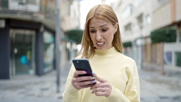 年轻的金发女人在街上用带有严肃表情的智能手机 — 图库视频影像