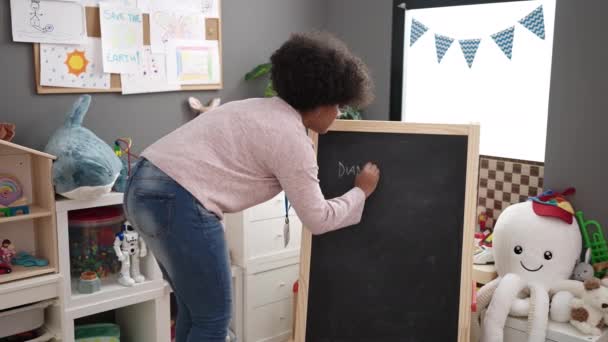 아프리카계 미취학 교사는 유치원에서 칠판에 이름을 자신감을 가지고 미소짓는다 — 비디오