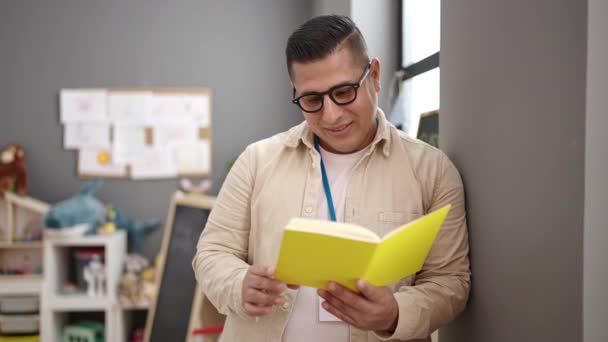 Young Hispanic Man Preschool Teacher Reading Book Standing Kindergarten — Vídeo de Stock