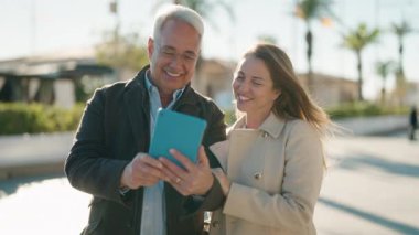 Orta yaşlı çift parkta video görüşmesi yaparken gülümsüyor.