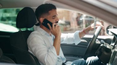 Young arab man talking on smartphone sitting on car at street
