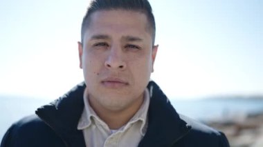 Deniz kenarında ciddi bir ifadeyle duran İspanyol genç adam.