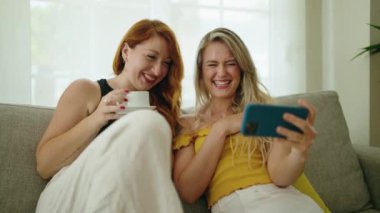 İki kadın evde akıllı telefondan kahve içip video izliyorlar.
