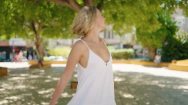 Parkta kendine güvenen genç sarışın kadın gülümsüyor.