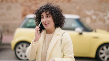 Gülümseyen genç bir kadın caddedeki akıllı telefondan konuşuyor.
