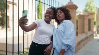 Afrika kökenli Amerikalı kadınlar anne ve kız sokakta akıllı telefonla selfie çekiyorlar.