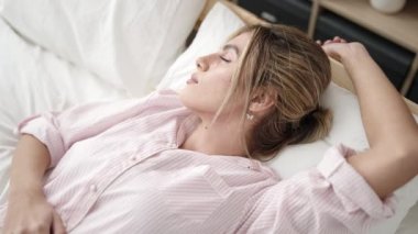 Genç sarışın kadın yatakta uzanıyor, yatak odasında uyuyor.