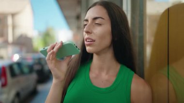 Genç, güzel, İspanyol bir kadın gülümsüyor ve caddede akıllı telefondan konuşuyor.