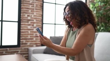 Orta yaşlı İspanyol kadın akıllı telefon kullanıyor ve kutlama yapıyor.