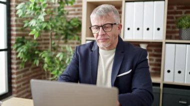 Orta yaşlı, kır saçlı, iş adamı. Ofiste dizüstü bilgisayar kullanıyor.