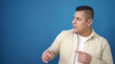 Genç İspanyol gülümseyen adam mavi arka planda kendine güvenen birini işaret ediyor.