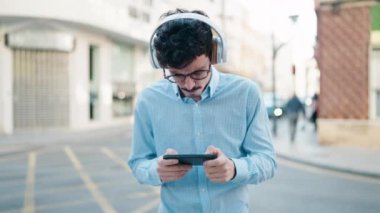 Young hispanic man smiling confident playing video game at street