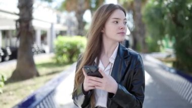 Parkta akıllı telefon kullanan genç sarışın kadın.