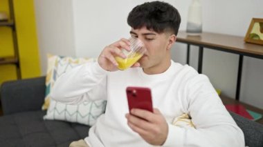 Genç İspanyol adam akıllı telefon kullanıyor. Evde portakal suyu içiyor.