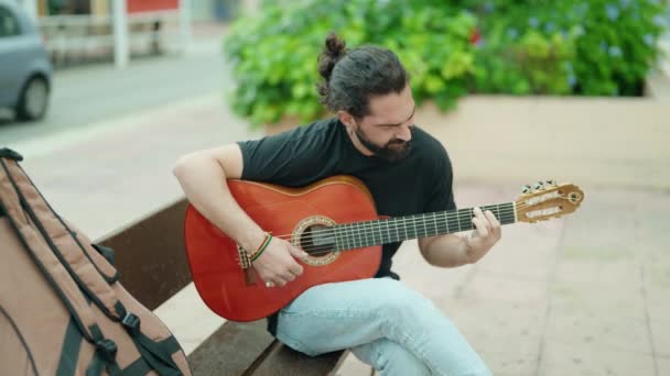 若いですヒスパニック男ミュージシャン遊び古典的なギター座っていますベンチに公園 — ストック動画