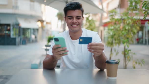 コーヒーショップのテラスでスマートフォンやクレジットカードを使っている若いヒスパニック系の男性 — ストック動画