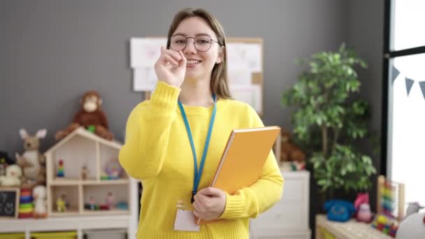 Young Blonde Woman Preschool Teacher Smiling Confident Holding Books Kindergarten — Wideo stockowe
