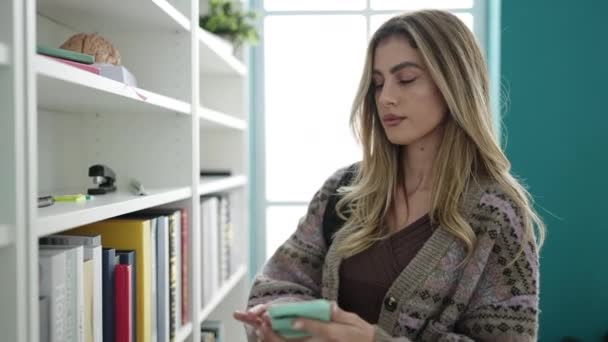 Joven Estudiante Rubia Usando Smartphone Sosteniendo Libro Biblioteca Universidad — Vídeos de Stock