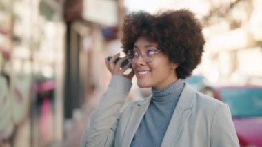 Afro-Amerikalı kadın gülümsüyor. Caddedeki akıllı telefondan kendine güvenen sesli mesaj dinliyor.