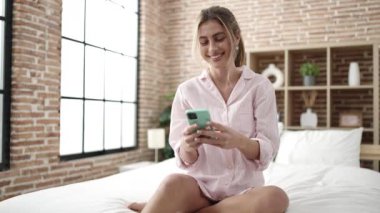 Yatak odasında akıllı telefon kullanan genç sarışın kadın.