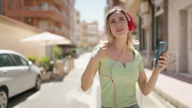 Kendine güvenen genç bir kadın müzik dinliyor ve sokakta dans ediyor.