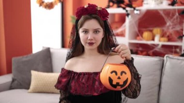 Young blonde woman wearing katrina costume holding halloween pumpkin basket at home