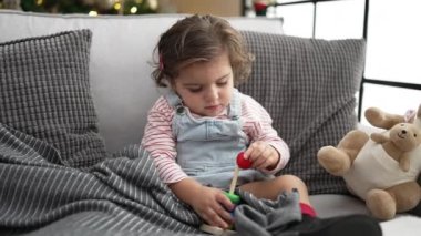 Adorable hispanic girl playing with hoops game sitting on sofa by christmas tree at home