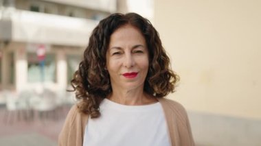 Orta yaşlı bir kadın sokakta kendine güvenerek gülümsüyor.