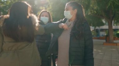Anne ve kızları sağlık maskesi takıyor. Parkta dirsek dirseği duruyor.