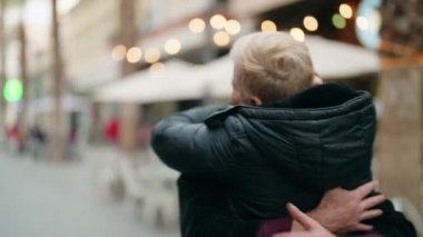 Anne ve oğul gülümsüyor. Kendilerine güveniyorlar. Sokakta sarılıyorlar.