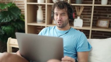 Young hispanic man having video call sitting on bed at bedroom