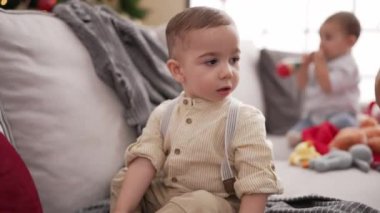 Evdeki Noel ağacının yanında kendinden emin gülümseyen iki bebek.