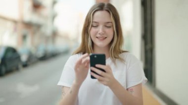 Beyaz bir kadın sokakta akıllı telefon kullanarak gülümsüyor.