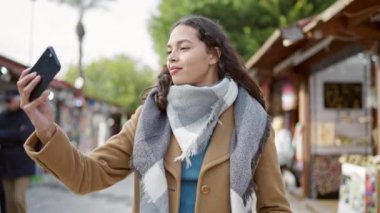 Genç, güzel, İspanyol bir kadın. Kendine güvenen bir gülümseme. Markette akıllı telefonun yanında selfie çekiyor.