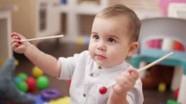 Anaokulunda elinde ksilofon çubuklarıyla yerde oturan sevimli çocuk.