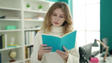 Young blonde woman student reading book doing silence gesture at library university