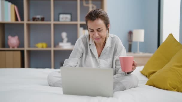 Kobieta Średnim Wieku Pomocą Laptopa Pije Kawę Siedząc Łóżku Sypialni — Wideo stockowe