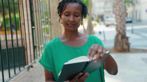 Африканская Женщина Средних Лет Улыбается Уверенно Читая Книгу Улице — стоковое видео