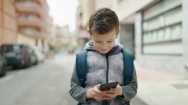 Sarışın çocuk sokakta akıllı telefon kullanıyor.