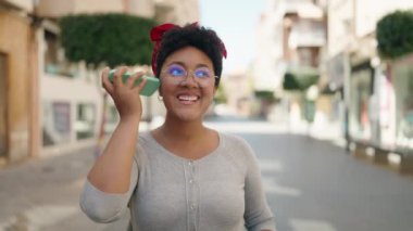 Afrika kökenli Amerikalı bir kadın akıllı telefondan sokakta yürürken sesli mesaj dinliyor.