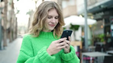 Young blonde woman smiling confident using smartphone at coffee shop terrace